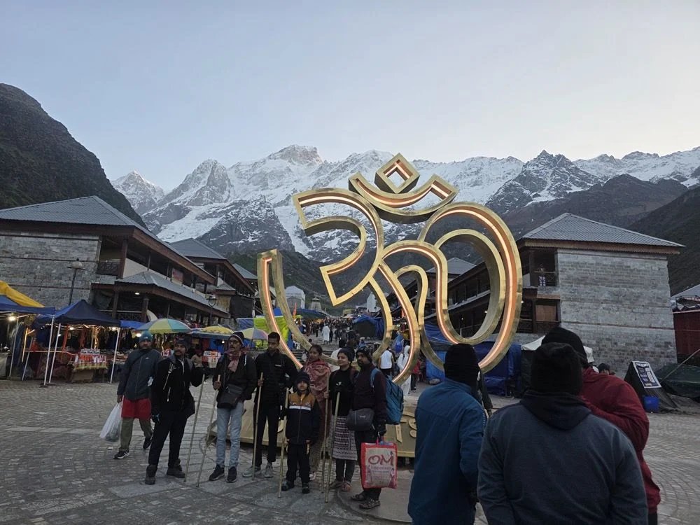 Golden Om sculpture at Kedarnath with Himalayan snow peaks at dawn